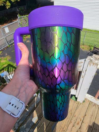 Customer's Thicc Buddy mug with a purple lid and a colorful, iridescent metallic scale pattern held in a hand outdoors.