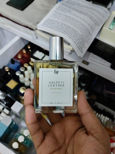 Customer's hand holding a square bottle of Halfeti Leather Eau De Parfum with a visible label in a drawer.
