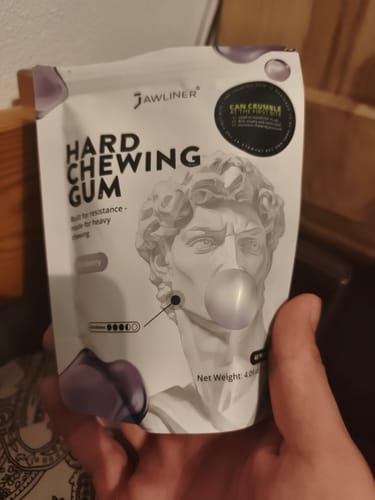 Customer's hand holding a white Jawliner Hard Gum pouch featuring a drawing of a statue blowing a bubble