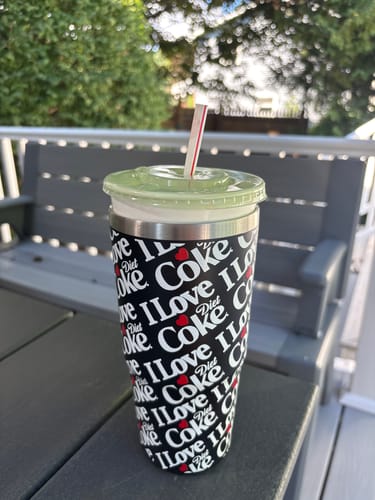 Customer's I Love Diet Coke To-Go Buddy cup with a straw, sitting on an outdoor table.