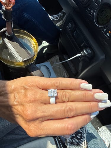 Customer's hand wearing the emerald cut silicone ring with a sparkling clear stone and white band inside a vehicle.