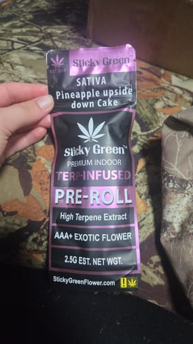 Customer's hand holding the black and purple Pineapple Upside Down Cake pre-roll packaging