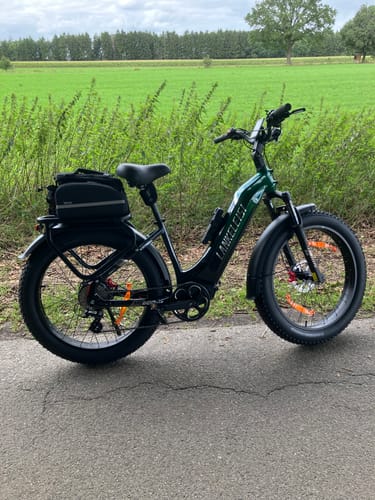 Customer's green Lankeleisi MG600 Plus fat bike with a rear bag parked on an asphalt path next to a field.