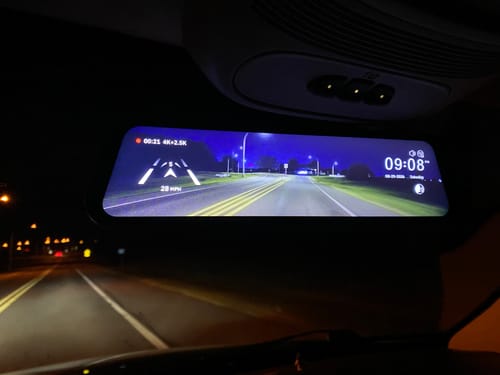 Reviewer's WOLFBOX G900TriPro rearview mirror screen displaying a night driving scene from a parked vehicle.
