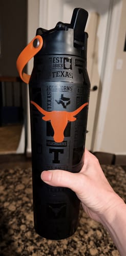 Customer's black 32oz Bottle Buddy with Texas Longhorns emblem, held in hand on granite countertop.