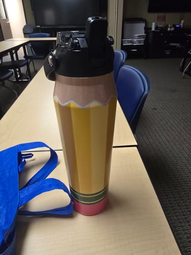 Customer's Bottle Buddy 32oz water bottle with a yellow pencil design, sitting on a classroom desk.