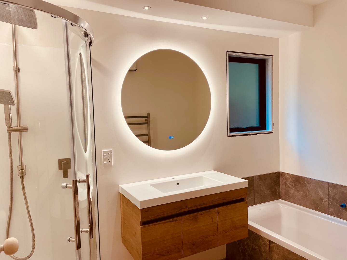 Customer installation photo from Laia C. showing a backlit Mirror World mirror with two round controls above a bathroom vanity