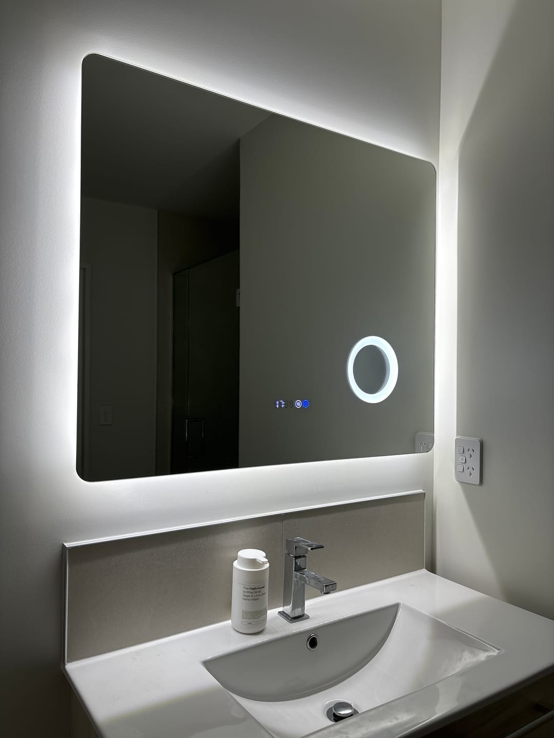 Customer installation photo from Lauren S. showing a rectangular Mirror World magnifier mirror with two round controls above a bathroom vanity