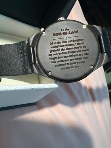 Close-up of a reviewer's black engraved watch, showing the message on the backplate for a son-in-law.