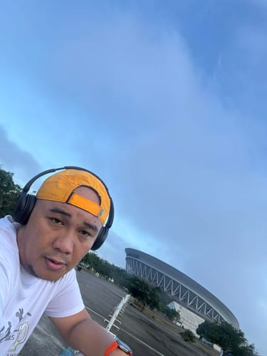 Reviewer wearing the yellow Nike Dri-FIT ADV Fly Cap backwards with headphones on, outdoors near a stadium.