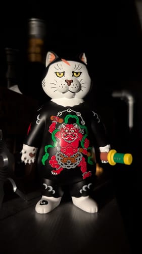 Customer's Donburi Toy figurine in dramatic lighting, showing the detailed red tattoo design on its black suit.