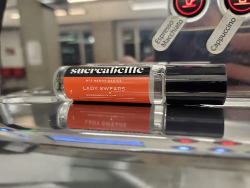 Customer's Lady Swears rollerball perfume resting on top of a metal coffee machine.
