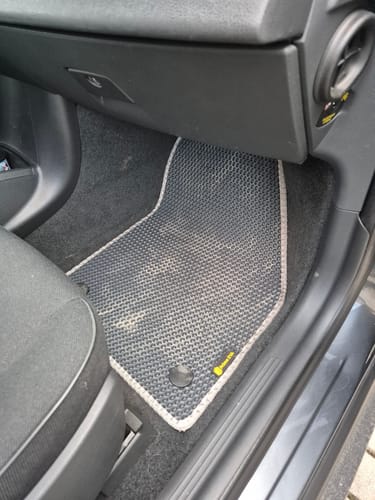 Recenzent pokazuje idealnie dopasowany, czarny dywanik samochodowy w przestrzeni na nogi pasażera.