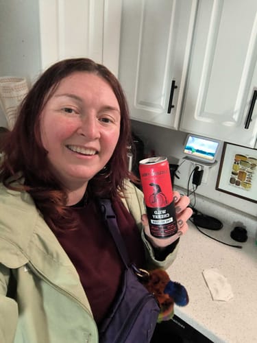 Reviewer smiling while holding a can of Wild Cherry THC Seltzer in a kitchen.