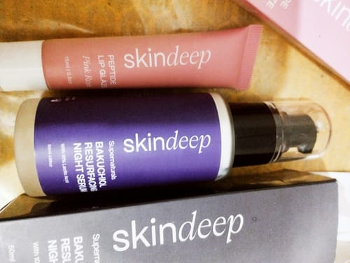 Reviewer's pink Skindeep Peptide Lip Glaze tube next to a bottle of Bakuchiol Night Serum.
