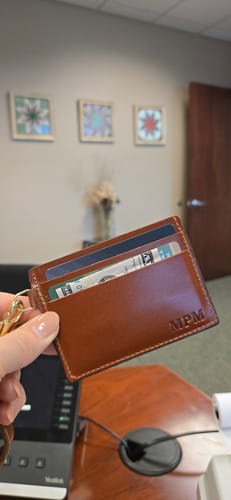 Customer holding the personalized brown Lucy wristlet wallet with cash and cards at an office desk.