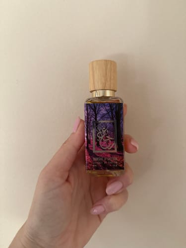A reviewer holds the Darkside of Saffron perfume bottle, showing its colorful label and wooden cap.