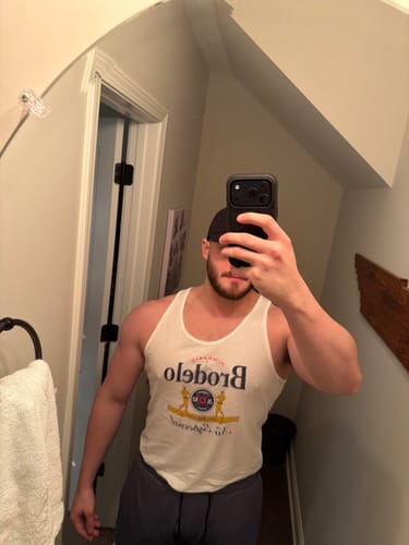 Reviewer in a mirror selfie showing the fit of the white BRODELO Tank Top.