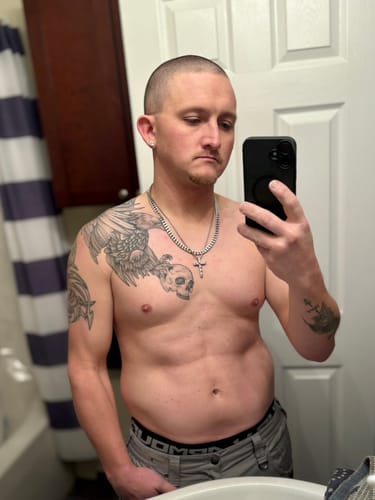 Customer takes a shirtless mirror selfie, showing their tan from the Bro Glo Body Tanner on their torso and arms.