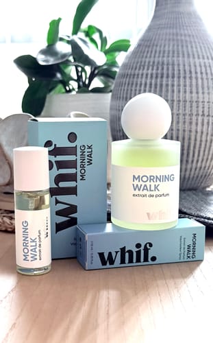 Reviewer's full-size and travel-size bottles of Morning Walk perfume shown with their light blue packaging on a table.