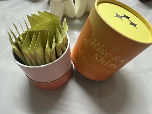 Customer's NMN Rise & Shine supplement shown with its orange cylindrical packaging and individual green sachets in the box.