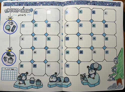 Customer's open journal showing a December 2025 calendar spread decorated with cute penguin stickers from the subscription.