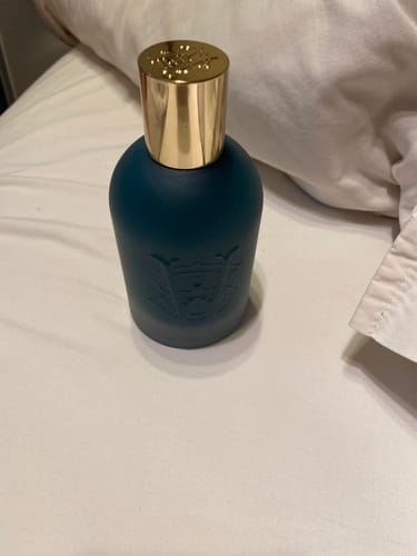 Customer's Figaro perfume in a dark teal bottle with a shiny gold cap, resting on a white surface.