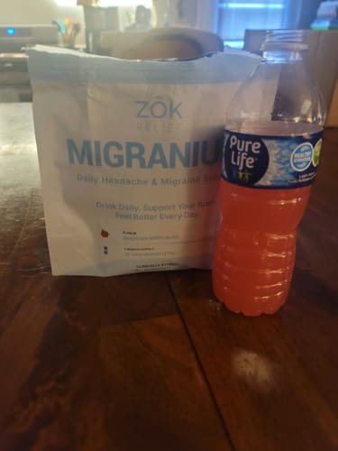 Customer's pouch of Migranium sitting on a table next to a water bottle with the prepared drink.