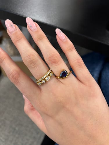 Customer's hand wearing the gold Pia Birthstone Ring with a dark blue pear-cut stone on their ring finger.