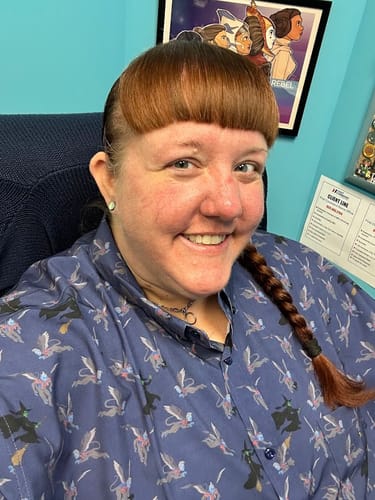 Customer smiling while wearing the blue "Fly! Fly! Fly!" shirt, showing its detailed flying monkey and witch pattern.