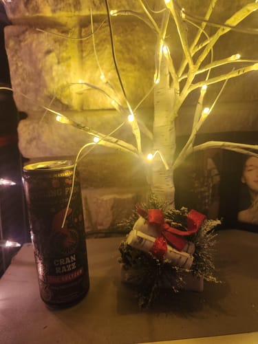 Customer's can of Cran Razz THC Seltzer on a table next to a small, decorative tree with warm lights.