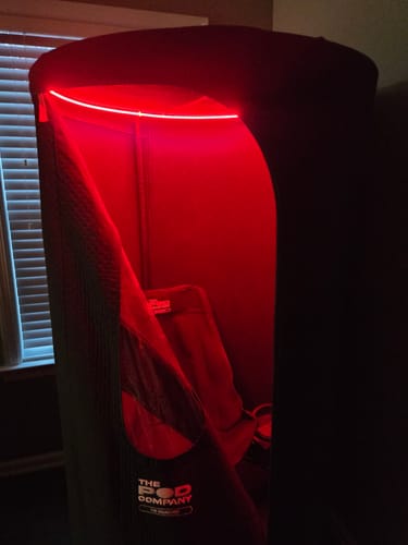 Reviewer's Sauna Pod 2.0 set up indoors, showing the interior illuminated by its bright red light.