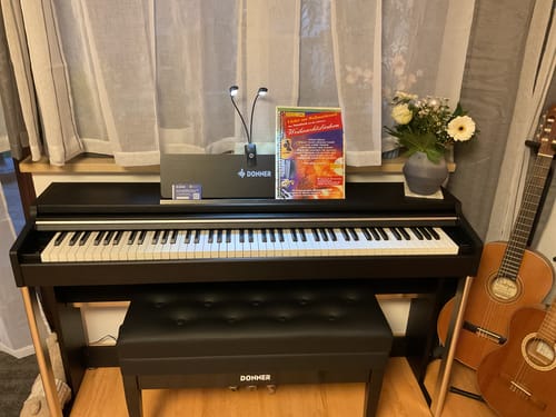 Ein Rezensent zeigt das edle Donner DDP-200 PRO Digitalpiano mit passender Bank, aufgebaut in einem Zimmer.