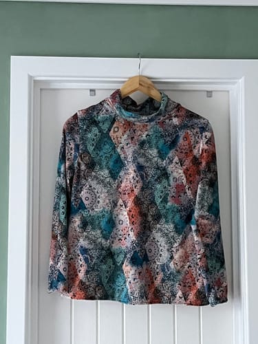 Customer's long-sleeved, high-neck top made from the colorful Boho Dreams Stretch Velvet Fabric, hanging on a door.