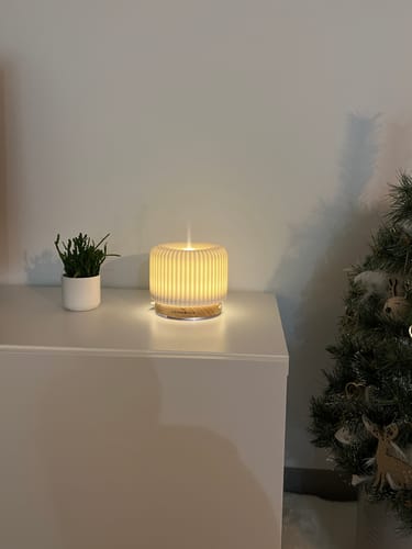 Recensent toont de Live Slow Aroma Diffuser met de verlichting aan op een wit kastje.