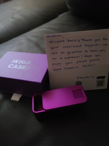 Customer's open purple Nano Case next to its matching box and a handwritten thank you note on a leather surface.
