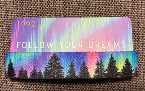 Reviewer's colorful Follow Your Dreams bracelet featuring a pine tree and aurora borealis design, shown with its matching card.
