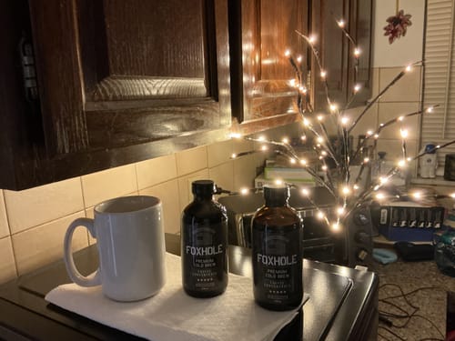 Reviewer's two bottles of Foxhole Coffee Concentrate on a kitchen counter next to a plain white mug.