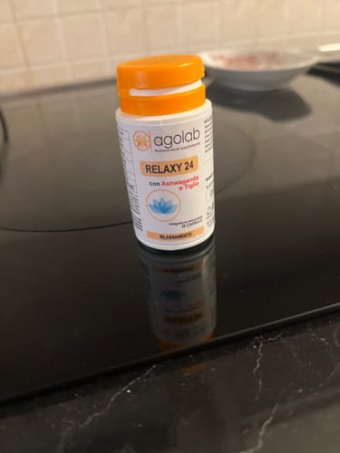 Recensore mostra il flacone bianco di Relaxy 24 con tappo arancione, posato su un piano cottura nero.