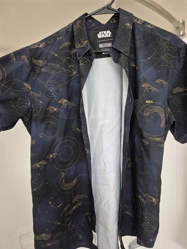 Reviewer's unbuttoned Star Wars 'Purrgil' shirt on a hanger, displaying its dark fabric and gold line-art pattern.