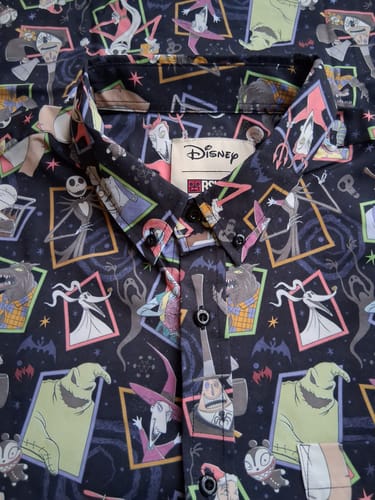 Reviewer's close-up of the 'Nightmare Neighbors' shirt, showing the colorful, detailed character pattern around the collar.