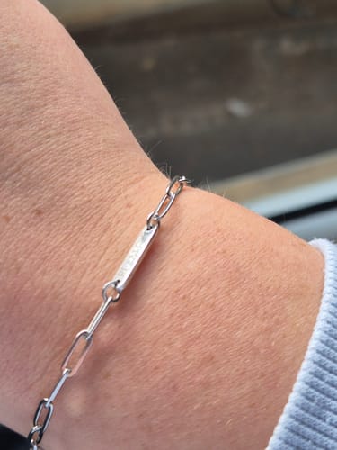 Close-up of a customer's wrist wearing the silver-colored Aurora bracelet with its engraved pendant.