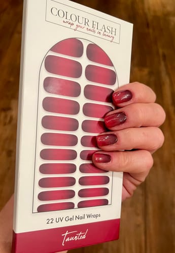 Eine Kundin hält die Verpackung der 'Taunted' UV-Gelfolien und zeigt ihre passende Maniküre mit Farbverlauf.
