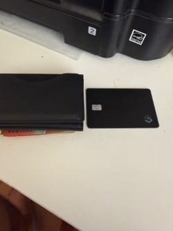Customer's black SPOTMINDERS Tracking Card sitting next to a compact black wallet on a desk.