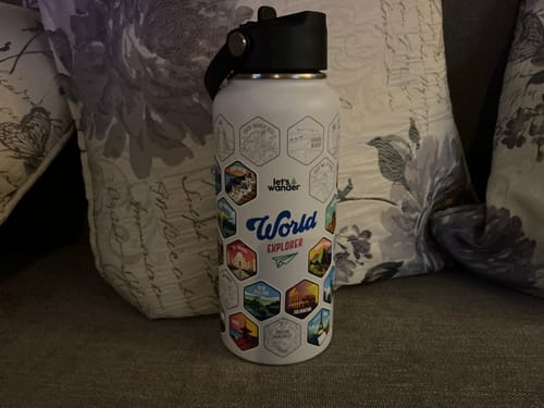 Customer's white World Explorer Bottle with colorful destination stickers applied, sitting on a couch.