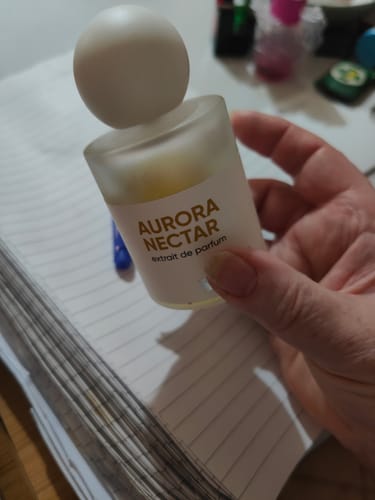 A customer holds the frosted glass bottle of Aurora Nectar perfume, with its white spherical cap.