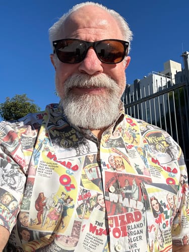 Reviewer outdoors wearing the 'Silver Screen Spectacle' shirt with a colorful collage of 'The Wizard of Oz' posters.