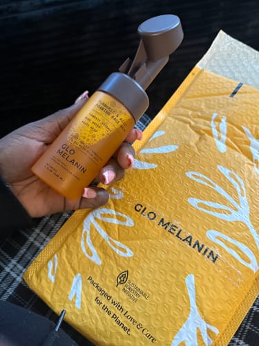Customer holding a bottle of Turmeric and Kojic Foaming Face Wash next to its yellow packaging.