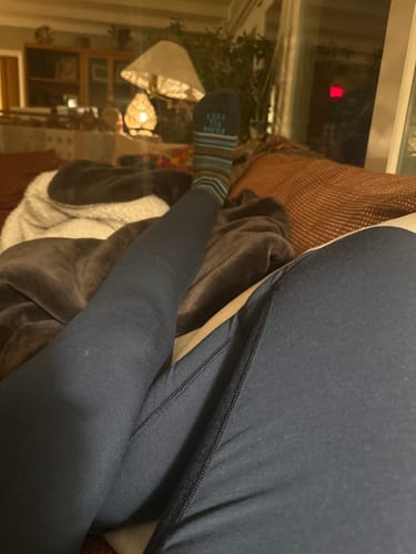 Customer relaxing on a couch in their deep navy Piper Pocket Leggings.