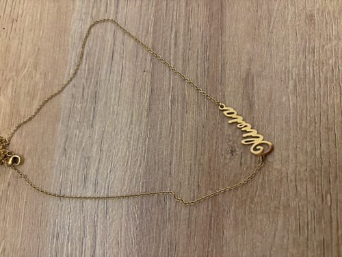 Customer's gold Signature Name Necklace with a script name, laid out on a wooden surface.